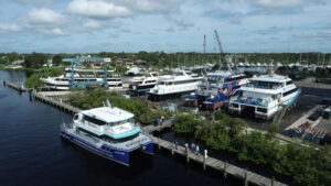 The Sadie Ann research vessel is docked among yachts at the tree-lined marina shore.