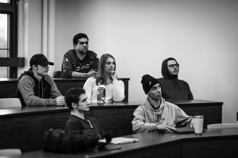 Six students sit in an economics classroom, listening attentively to something out of the frame.