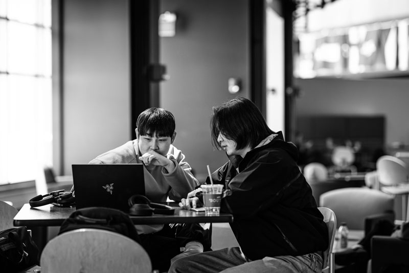 Two people sit at a table, discussing international business while looking at a laptop together.
