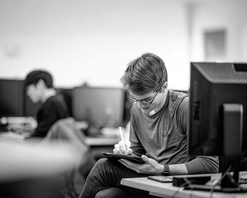 Person solving mathematics problems with a stylus on a tablet in a busy office setting.