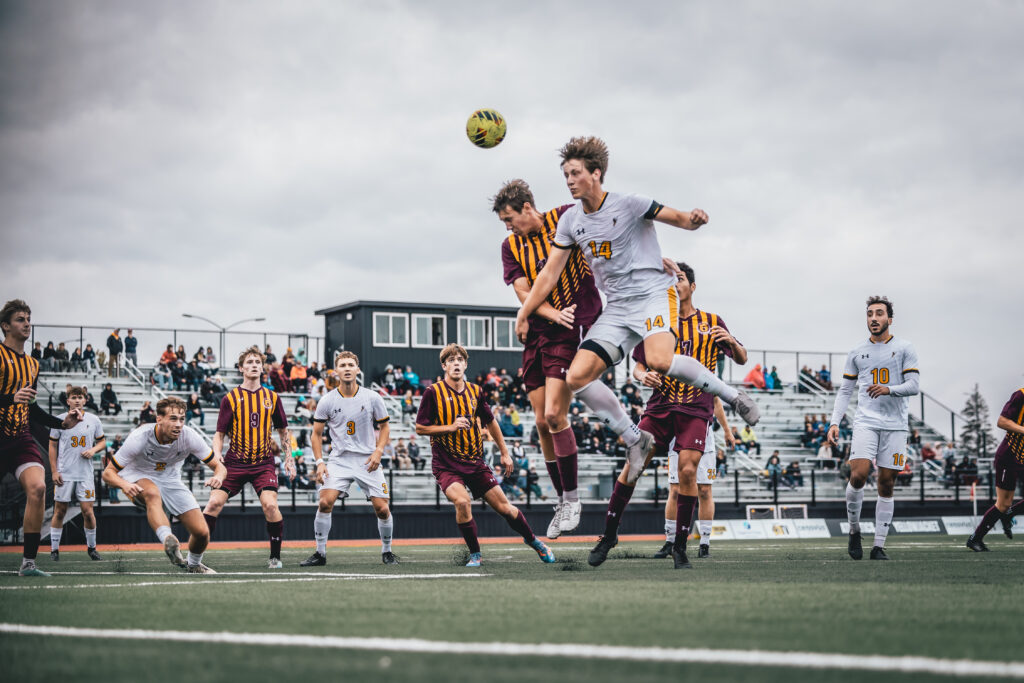 Men's soccer game. Player jumping in the air headbutting soccer ball with stadium full of fans watchin in the background.