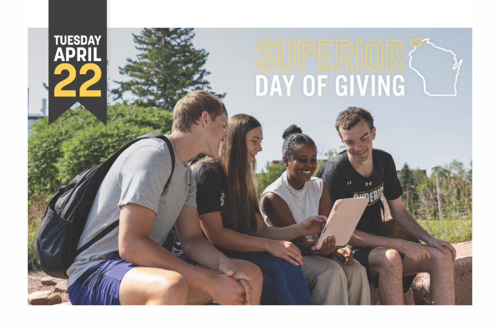 Superior Day of Giving - Tuesday, April 22, 2025. Four students sitting on a rock wall looking at an ipad smiling.