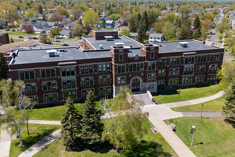 Aerial view of a large brick school building with trees and walkways in front.