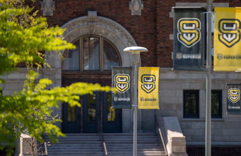 Banners with SU logo and SUPERIOR hang in front of a brick building with arched doorway.