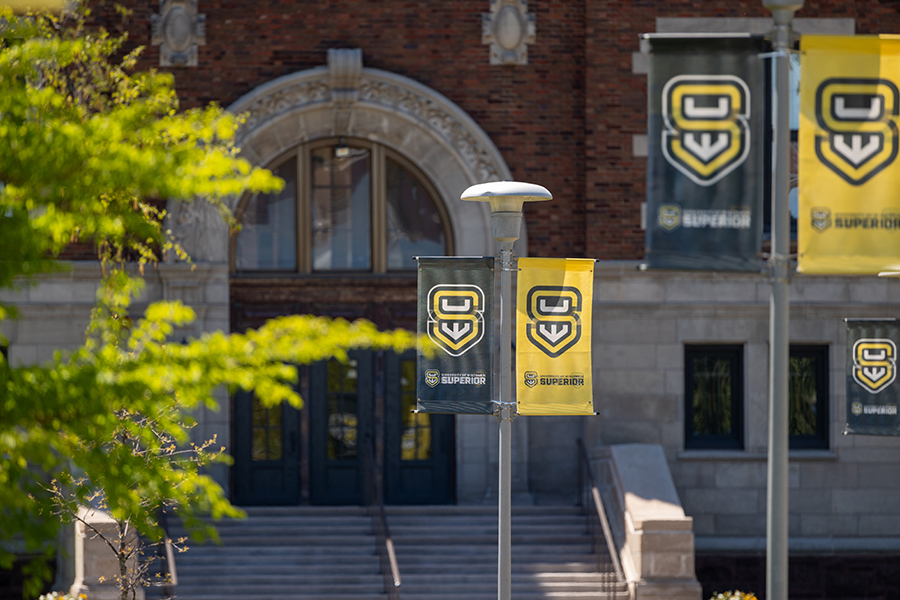 Banners with SU logo and SUPERIOR hang in front of a brick building with arched doorway.
