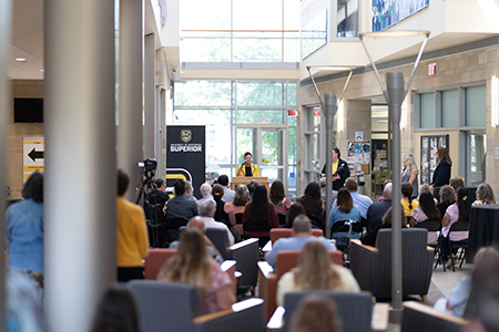 A speaker addresses an audience seated in a bright, modern indoor event space.