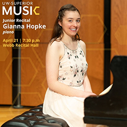 Young woman in a light floral dress sits at a grand piano, smiling at the camera.
