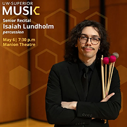 Person in black suit holding percussion mallets, standing in front of a wood-paneled background.