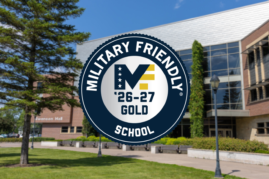 A gold Military Friendly School 26-27 badge is displayed over an image of a college campus with trees, grass, and a modern brick building under a blue sky.