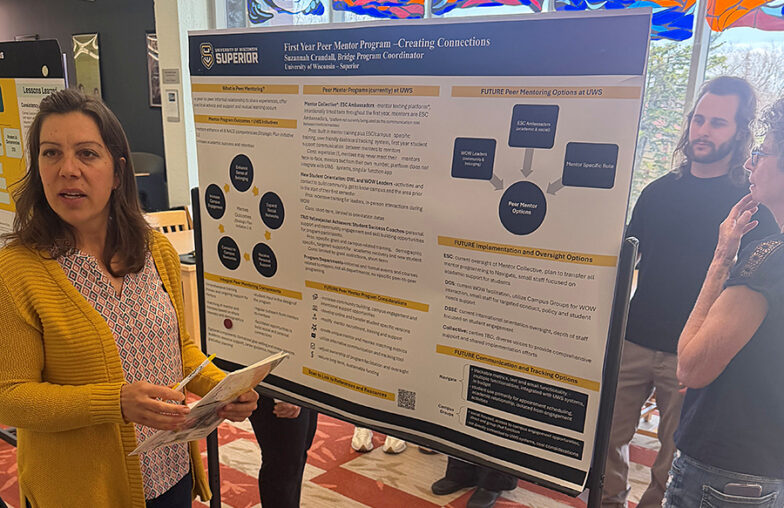 A woman presents a research poster to three people at an indoor academic event.