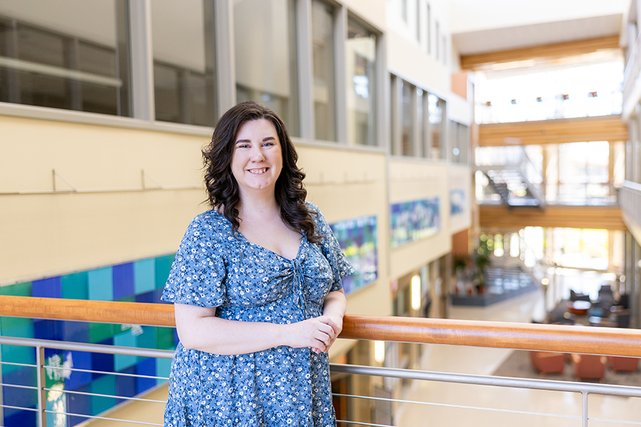 Woman in a blue floral dress standing by a railing in a bright, modern indoor atrium.