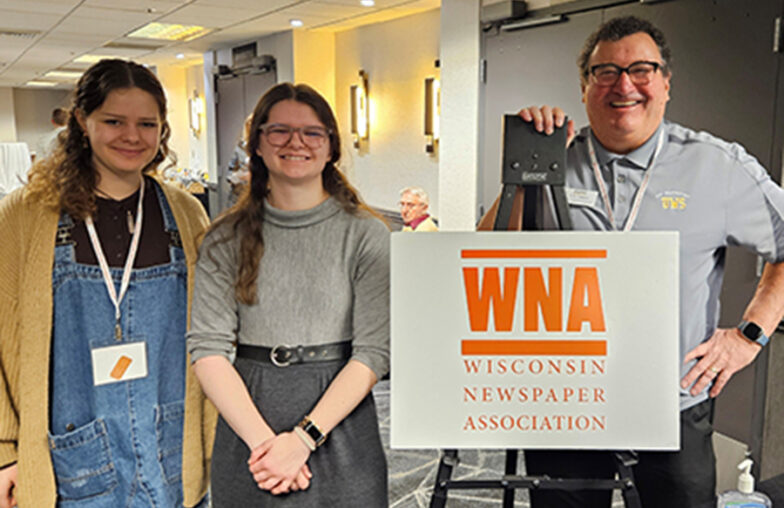Three people stand indoors next to a sign that reads WNA Wisconsin Newspaper Association.