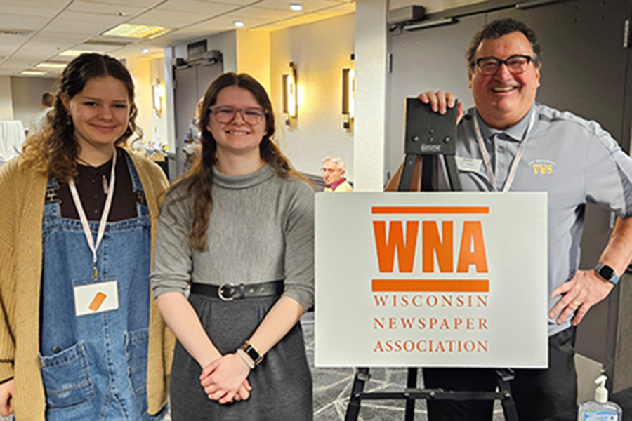 Three people stand indoors next to a sign that reads WNA Wisconsin Newspaper Association.