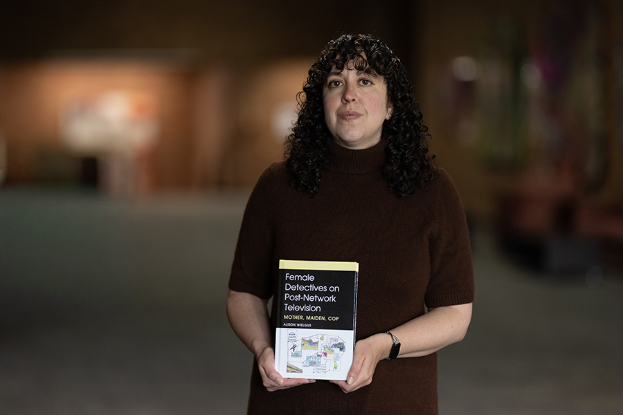 A person with curly hair holds a book titled Female Detectives on Post-Network Television.