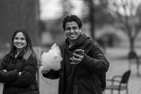 A man with a phone and cotton candy smiles next to a woman; academic microcredentials context.