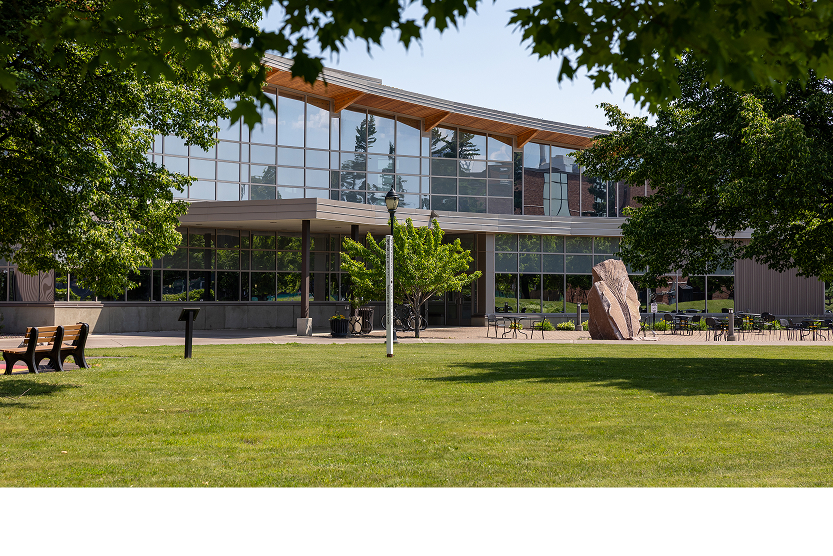 Yellowjacket Union, a modern glass building with wooden roof, near admissions, surrounded by lawn, benches and trees.