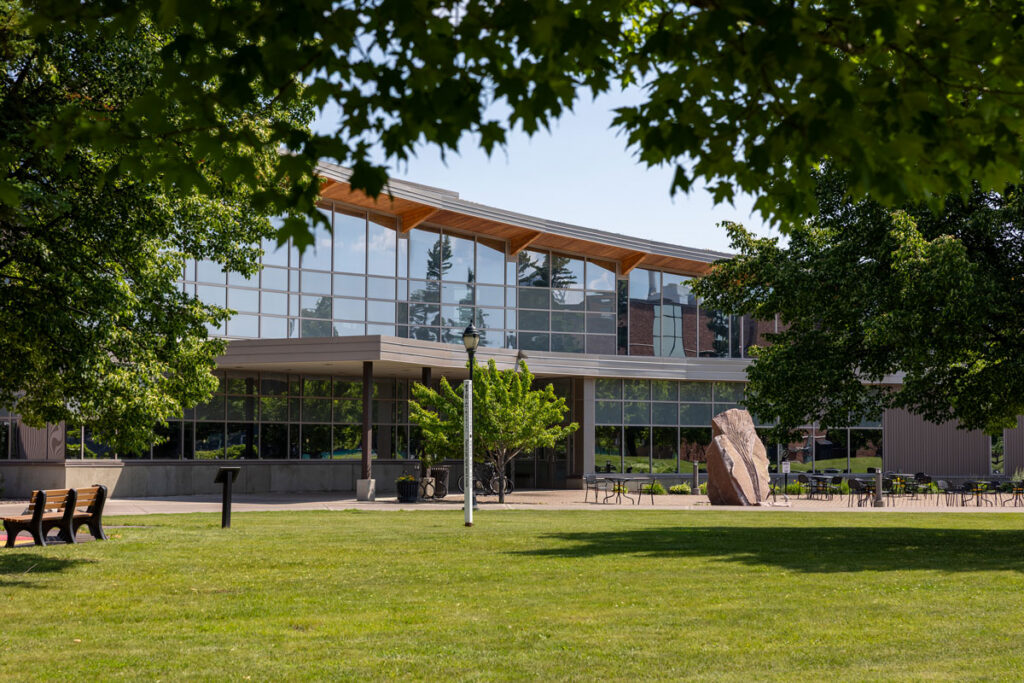 Yellowjacket Union with large windows, surrounded by trees and a grassy lawn with benches.