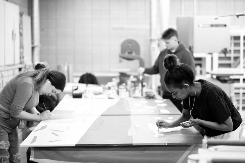 Four people engage in art education, working on large painting and drawing projects in a studio.