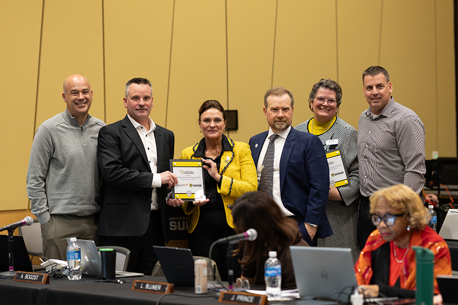 A group of people standing behind a table, one woman holding an award certificate.