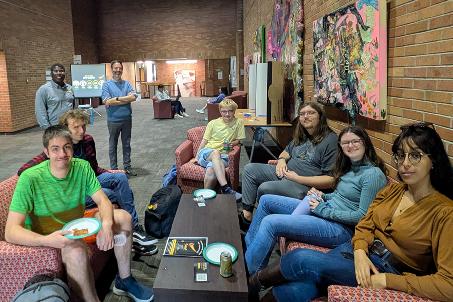 A group of students sitting in a lounge area with armchairs, a coffee table, and wall art.