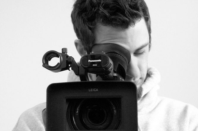 Person in a hoodie filming with a Panasonic video camera, exploring communication and media arts.