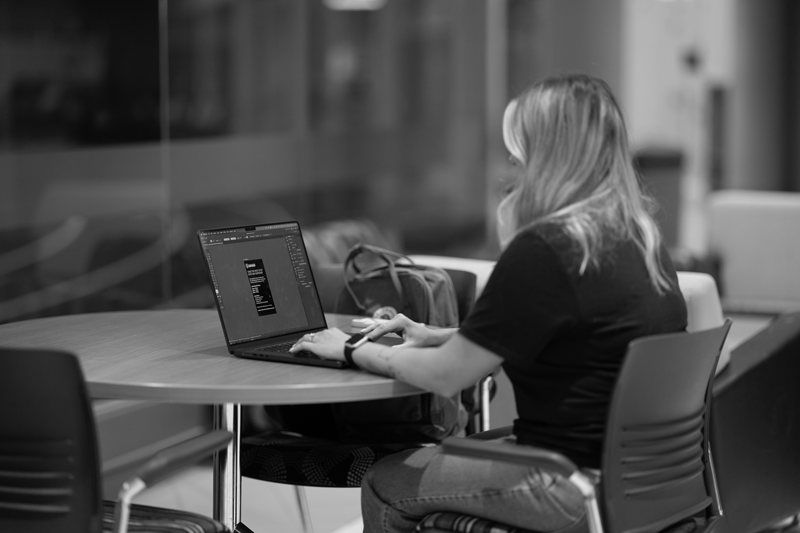 Student studying graphic design sits at a table with laptop working on an assignment.