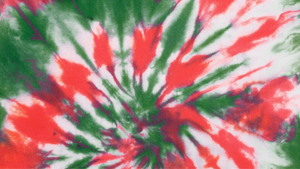 Tie-dye pattern featuring bold splashes of red, green, and white radiating outward in a circular, spiral design. The colors are vivid and blend slightly at the edges, creating a dynamic, festive look.