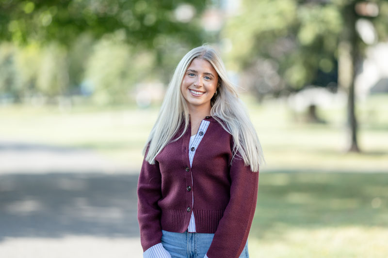 A smiling woman with long blonde hair wearing a maroon cardigan perfect for fall and spring.