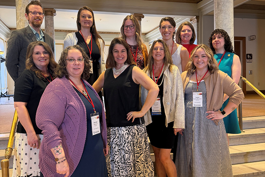 A group of eleven adults pose and smile together on a staircase in a formal indoor setting.