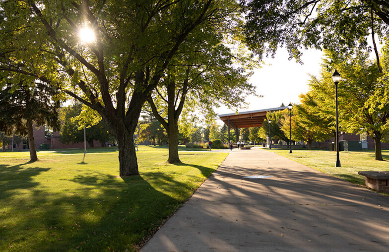 A concrete path leads through a park toward a pavilion on a sunny day.