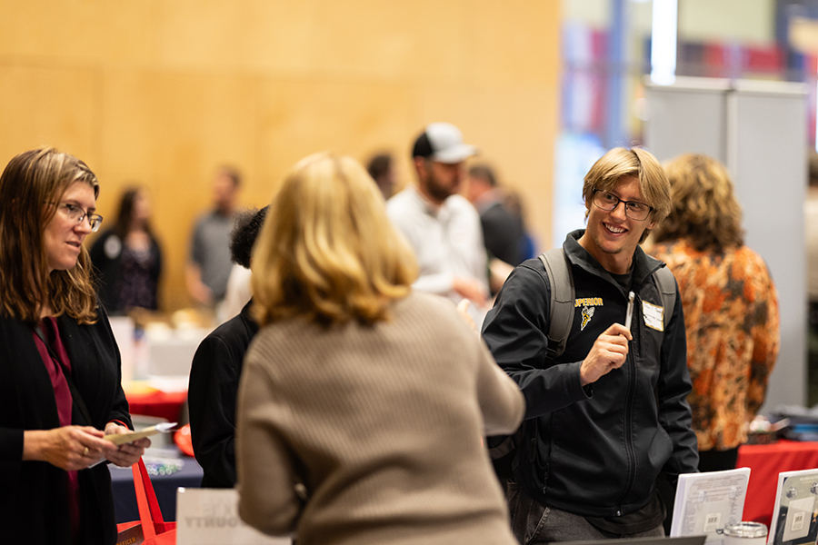 People talking and networking at an indoor event with tables and informational displays.