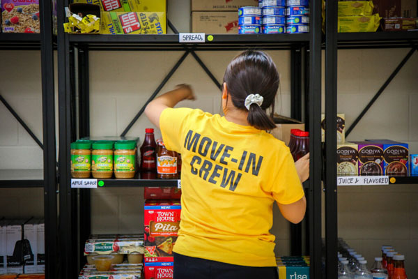 Person in yellow Move-In Crew shirt stocks shelves, showcasing UW-Superior sponsorship.