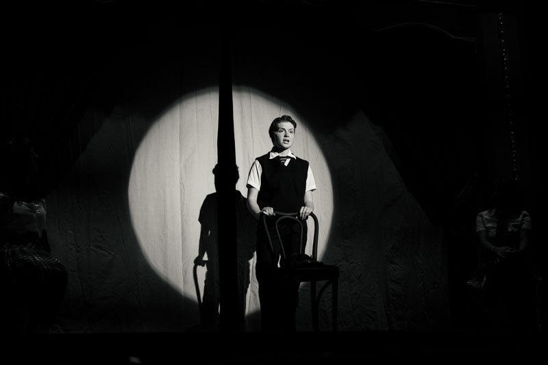 Person standing in a spotlight on stage, holding a chair, as if set for a filmmaking scene.