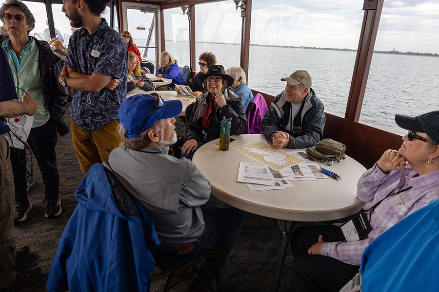 People sitting at a table on a boat, looking at maps and documents.