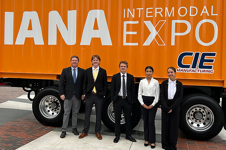 Five people in business attire stand in front of an orange intermodal expo trailer.