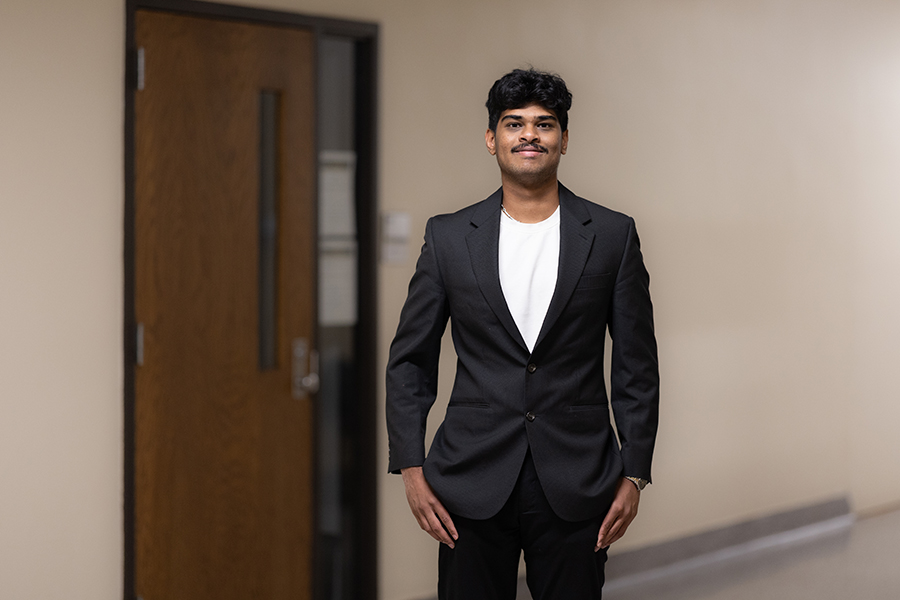 A young man wearing a black blazer and white t-shirt standing in a hallway.