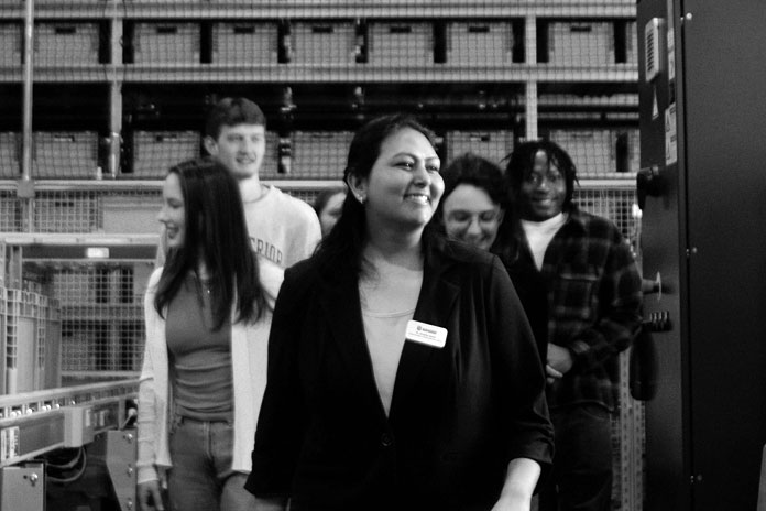 A woman leads a group through an industrial space, discussing supply chain management strategies.