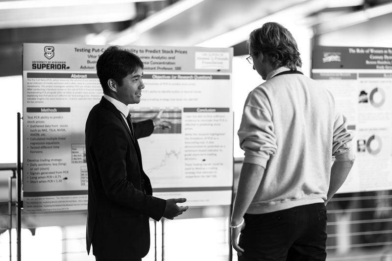 Two people discuss a business analytics research poster about stock prices at an academic event.