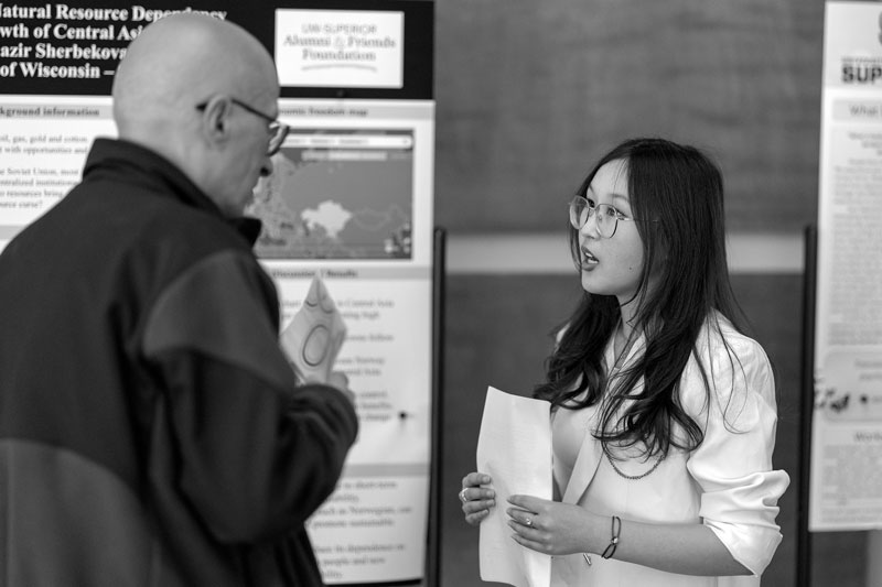 A woman speaks to a man about legal studies in front of research posters at an academic event.