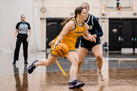 A basketball player in yellow dribbles past a defender in navy on an indoor court.
