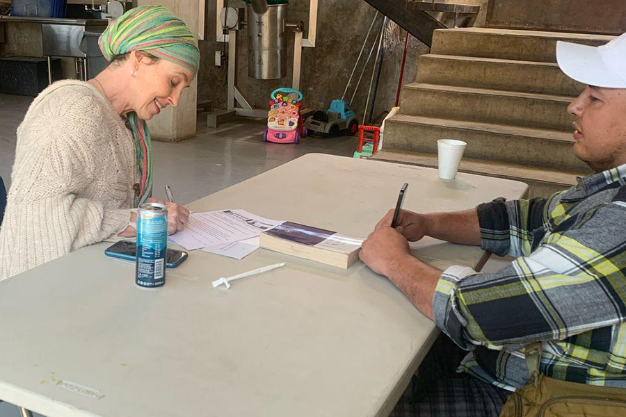 Two people sit at a table filling out paperwork with pens in an indoor setting.