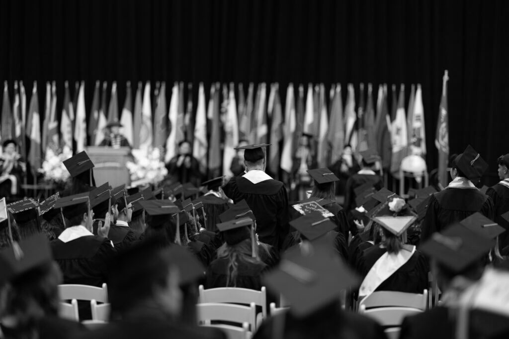 Graduation ceremony with graduates in caps and gowns seated facing the stage.