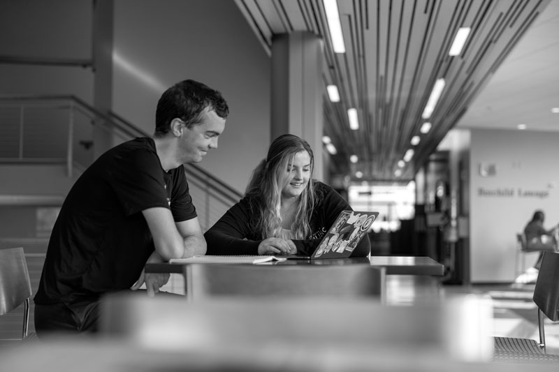 Two people discuss Pre-law at UW-Superior while looking at a laptop in a modern indoor setting.