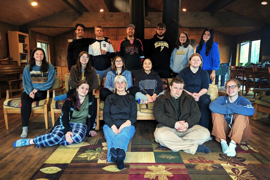 A group of fifteen people pose together indoors, some sitting and some standing, in a cozy room.