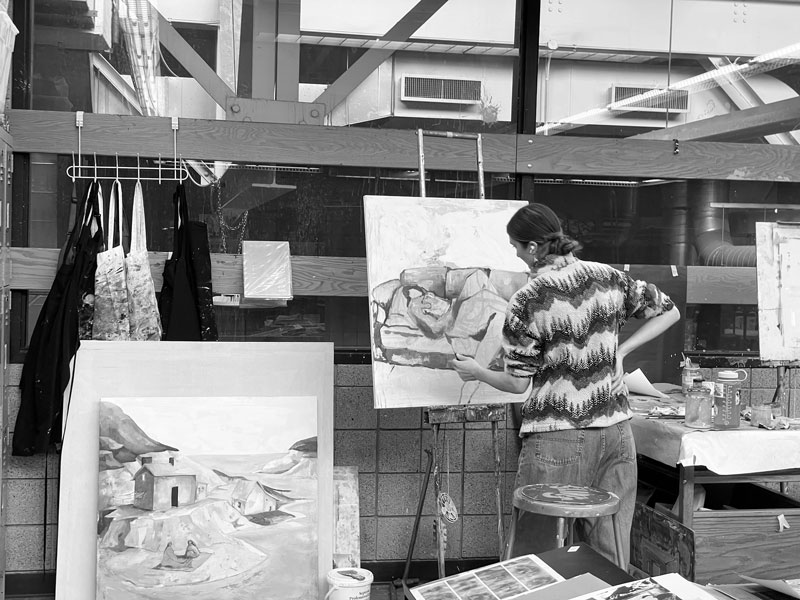Person painting an abstract image on canvas in an art studio, with finished works nearby.