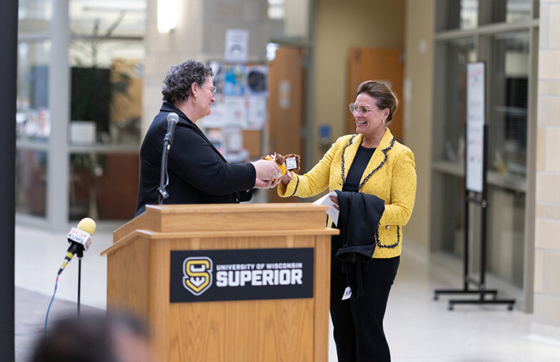 Two people exchange an item at a podium labeled University of Wisconsin Superior..