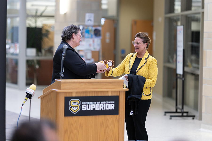 Two people exchange an item at a podium labeled University of Wisconsin Superior..
