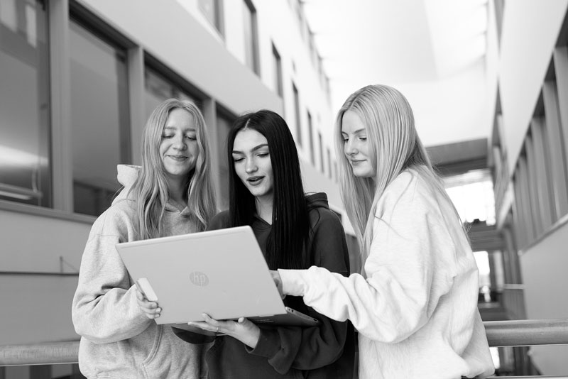 Three young women in hoodies discuss a communication degree at UW-Superior around a laptop.