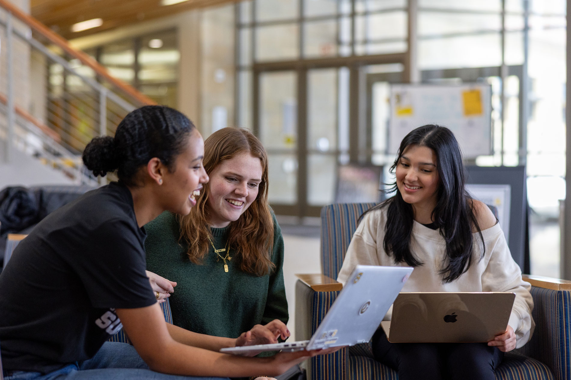 Three young adults sit indoors, smiling and working on Non-Profit Communications and Management.