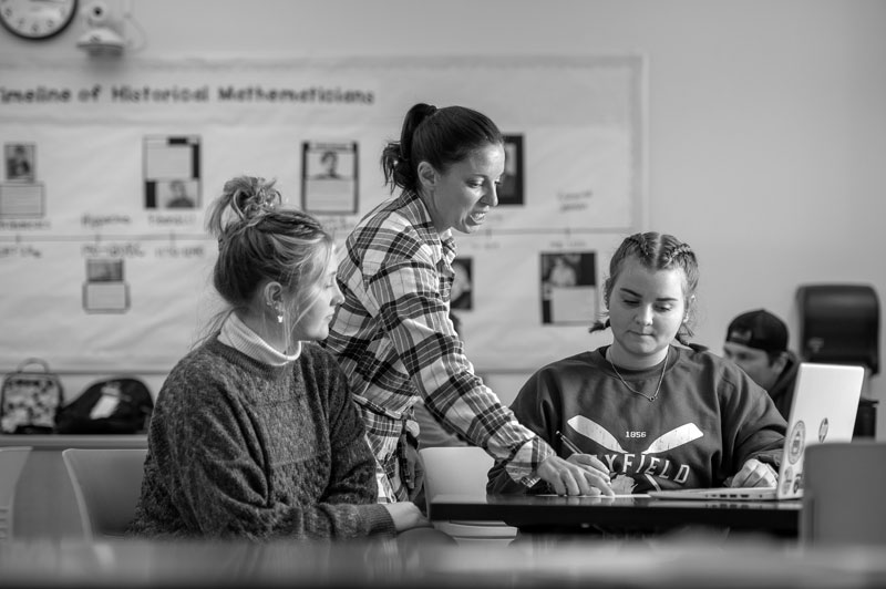 Teacher with a Bachelor's of Social Work assists two students at a table in a classroom.